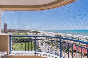 Ein Balkon mit einem Maschendrahtzaun, der Blick auf Strand, Meer und Stadt bietet.