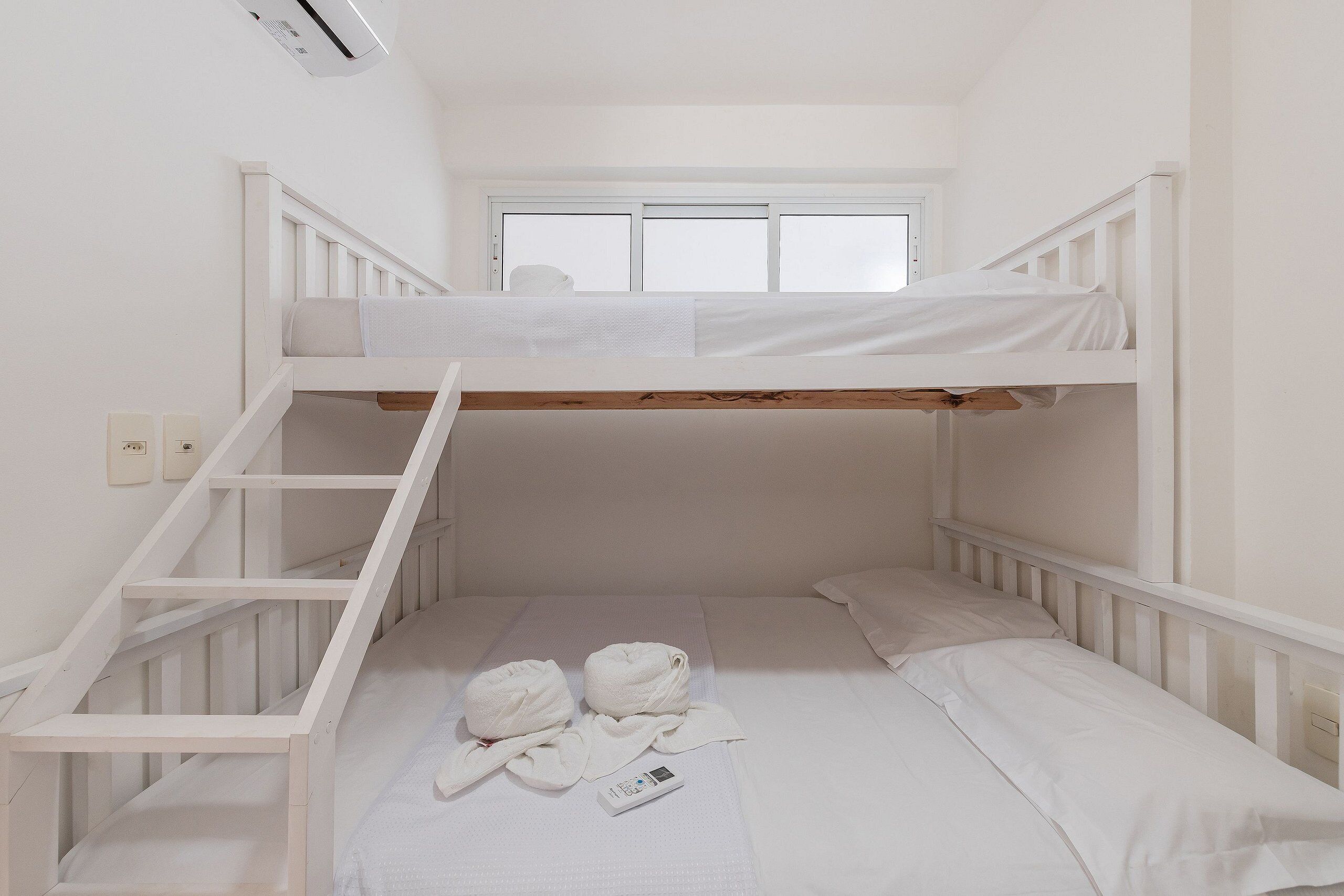 A bunk bed room with a window, a wooden ladder, and two towels on the lower bunk.