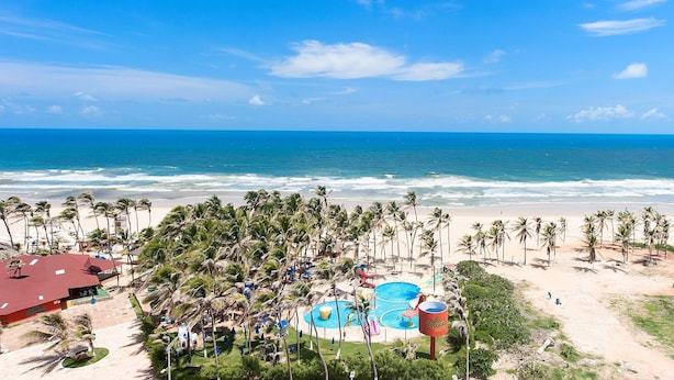 Um resort à beira-mar com palmeiras, área de piscina e vista para o oceano.