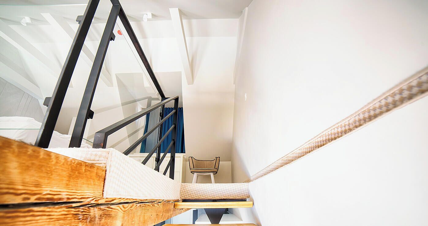 A narrow staircase with a wooden handrail and a chair at the bottom.