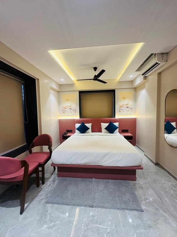Une chambre d’hôtel moderne dotée d’un grand lit, d’un ventilateur de plafond, d’un appareil de climatisation et d’un coin salon avec des fauteuils.