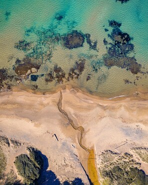 Luchtbeeld van een kustlandschap met helder water, zandgebieden en een smalle waterloop.