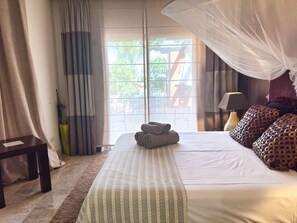 A hotel room with a bed, a bedside table, a lamp, a potted plant, and a view through the window. - Elegant Family Apartment in Aloha Golf Marbella (Marbella)