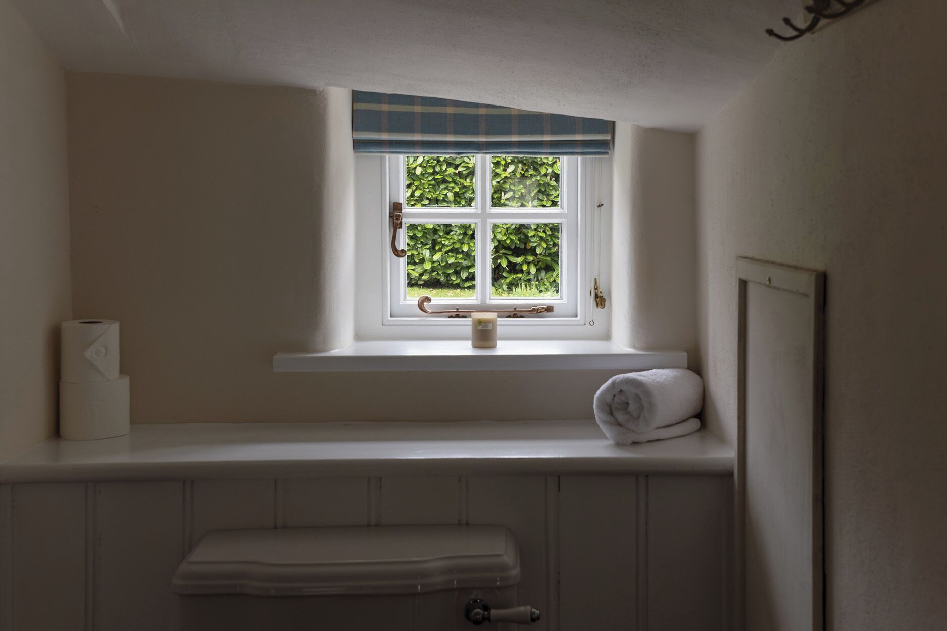 Ein Badezimmer mit Fenster, Handtuch und Toilettenpapierhalter.