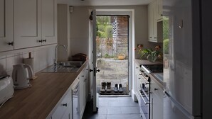Eine schmale Küche mit weißen Schränken, einer Holzarbeitsplatte und Blick auf einen Garten durch eine offene Tür.