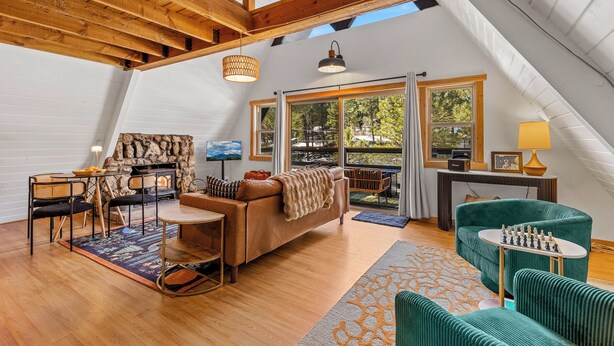 Un loft spacieux avec de hauts plafonds, des poutres apparentes, un coin salon confortable avec un canapé et des fauteuils, une table à manger et une table d’échecs.