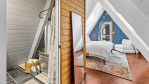 Une chambre avec un plafond en pente, un lit, une table de chevet et une fenêtre.