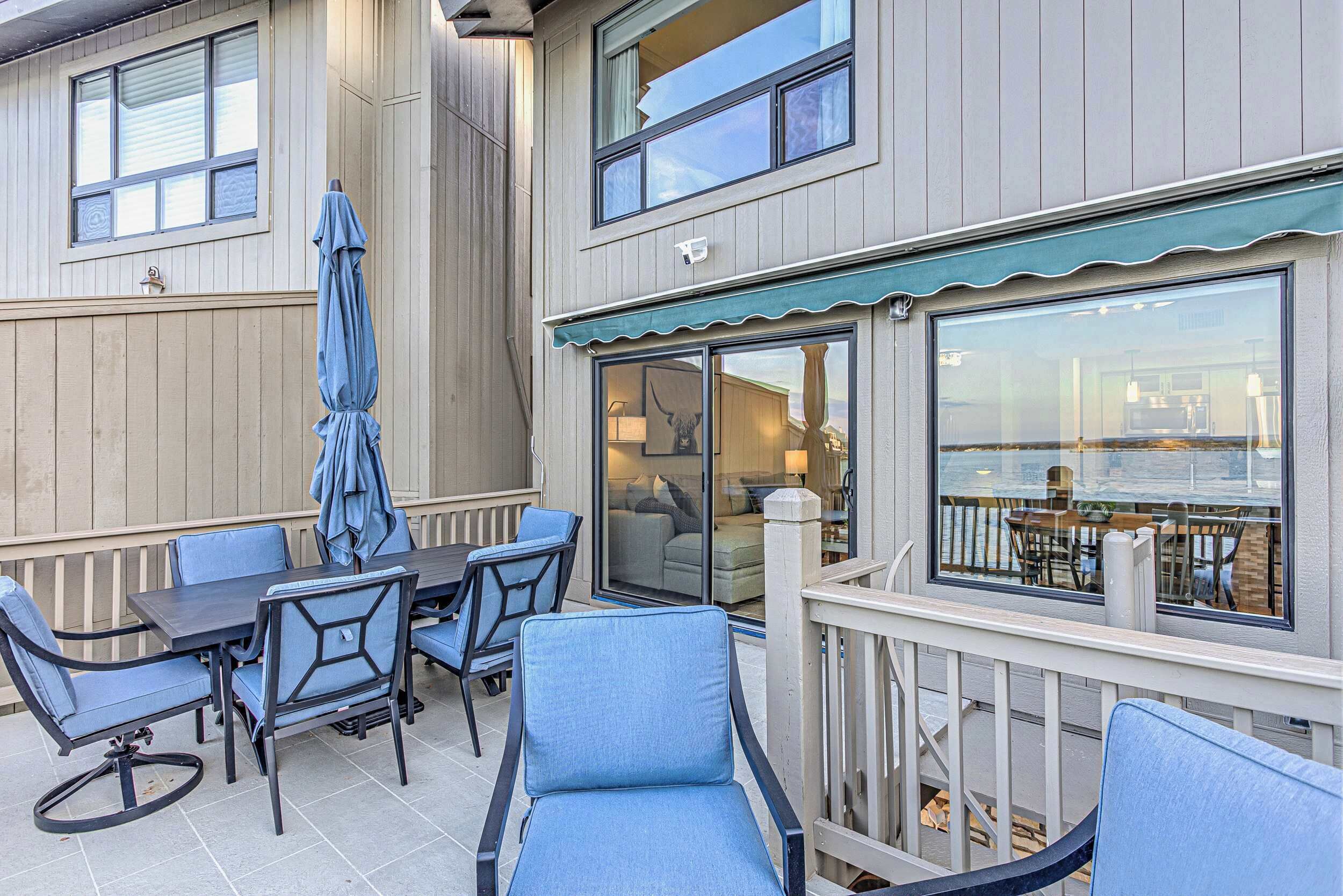 Un espace extérieur aménagé en terrasse, avec une table et des chaises, un parasol et une vue sur l’intérieur à travers une porte vitrée.
