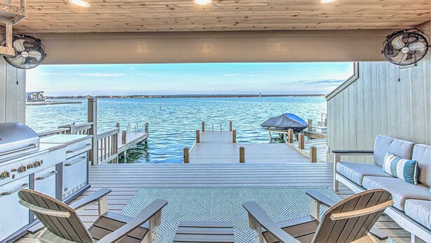 A wooden deck with a view of the water, a grill, and seating areas.