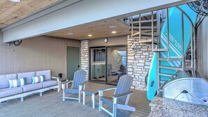 A covered outdoor area with a stone wall, a wooden ceiling, a sofa, two chairs, a surfboard, and a staircase.