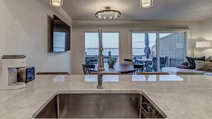 A modern kitchen with a stainless steel sink, a built-in coffee maker, and a dining area with a view of the ocean.