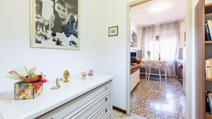 Une pièce avec une commode blanche, une photographie encadrée accrochée au mur, une petite table avec des chaises et une bibliothèque.