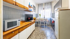Une cuisine compacte équipée d’un four à micro-ondes, d’un four et d’un réfrigérateur. On y trouve une table à manger avec des chaises, ainsi qu’une fenêtre avec des rideaux.