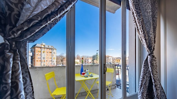 Un balcon avec des chaises jaunes et une table, une vue sur des immeubles et des rideaux à motifs.