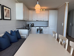 Ett modernt kök med vita skåp, ett matbord och en soffa med blå kuddar.