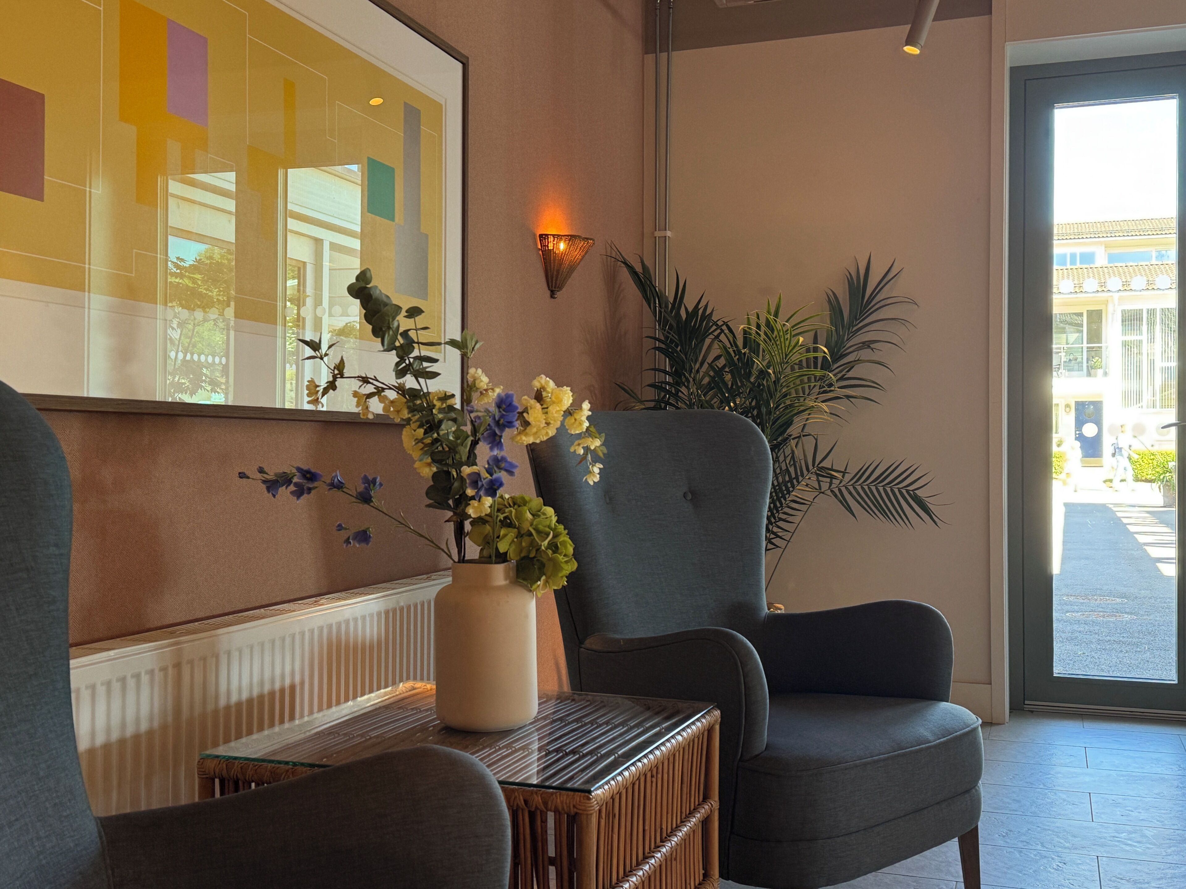 A modern interior with a seating area, a vase with flowers, a wall-mounted light, and a large window.