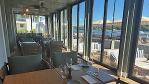 An indoor dining area with large windows, wicker furniture, and a view of the waterfront. - Havna Tjøme Apartments  (Faerder)