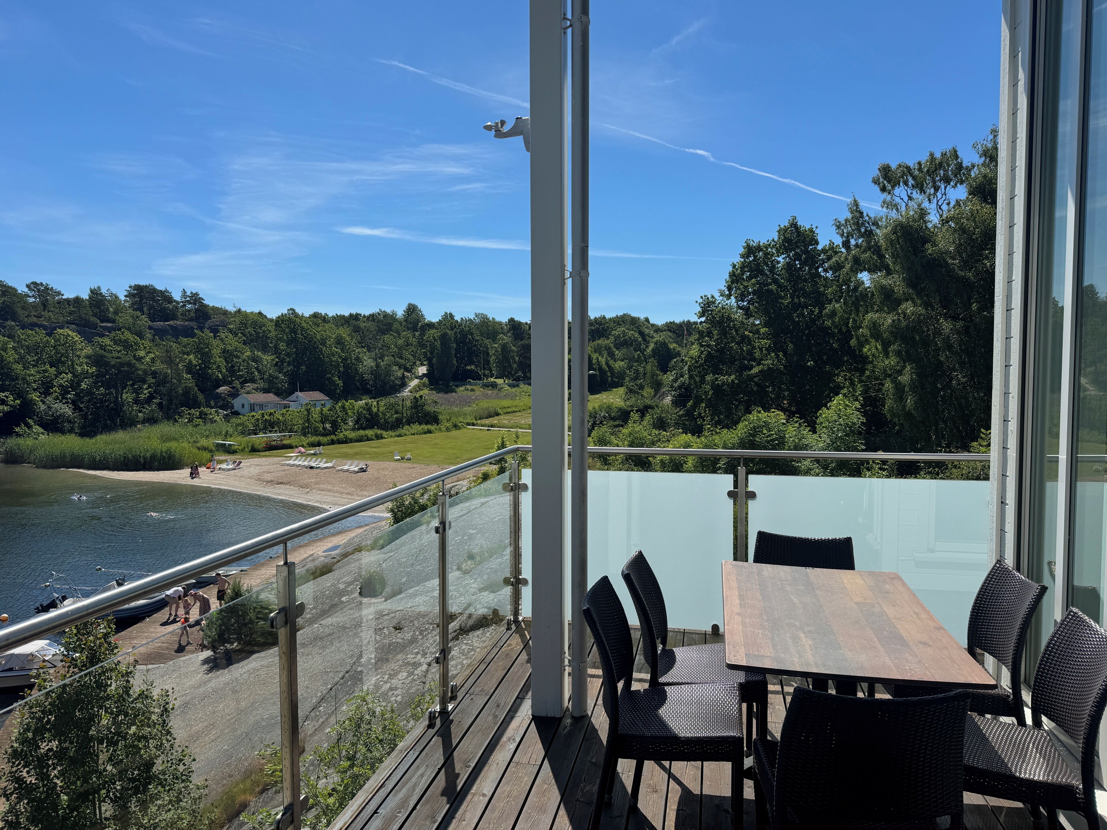 Un balcón con vista a un lago, mobiliario exterior y baranda de cristal.