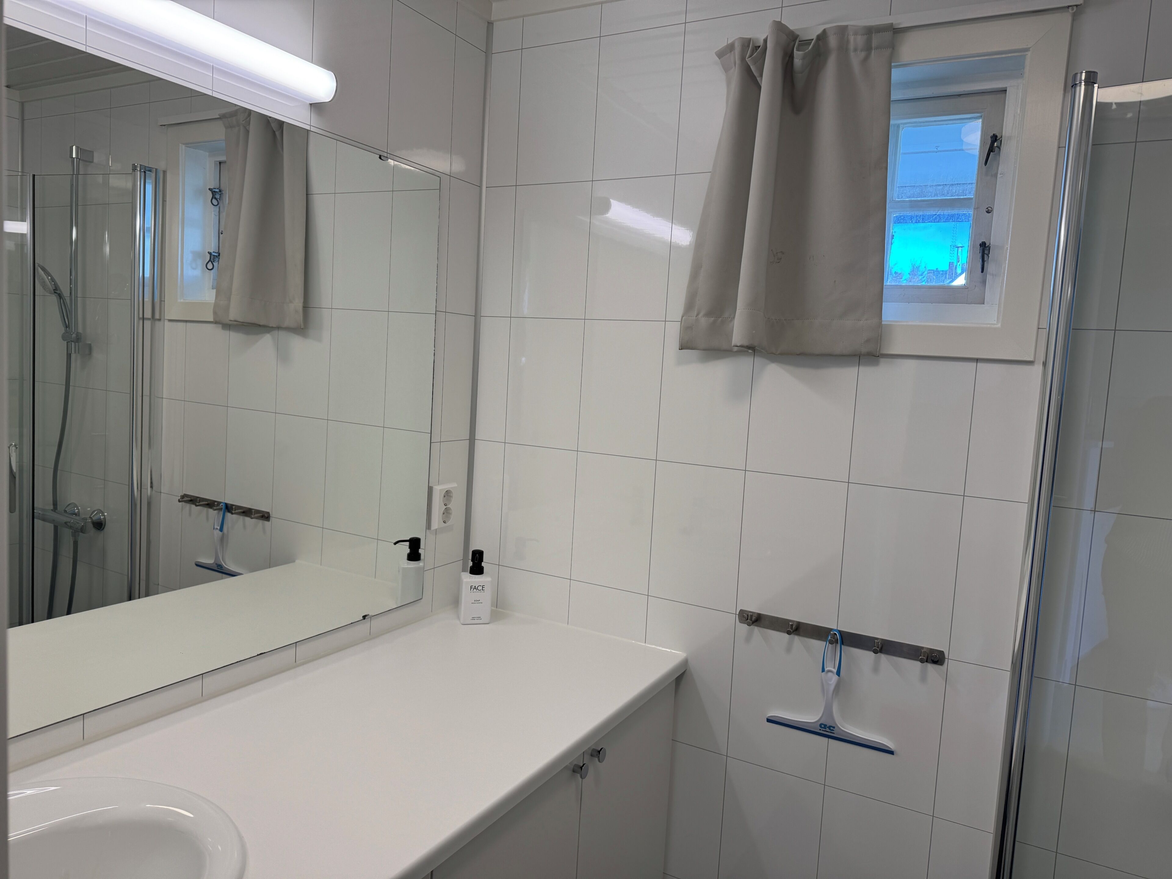 A bathroom with a glass shower enclosure, a white sink, a mirror, and a window with a view.