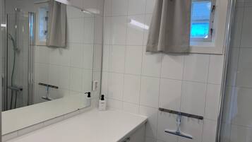 A bathroom with a glass shower enclosure, a white sink, a mirror, and a window with a view.