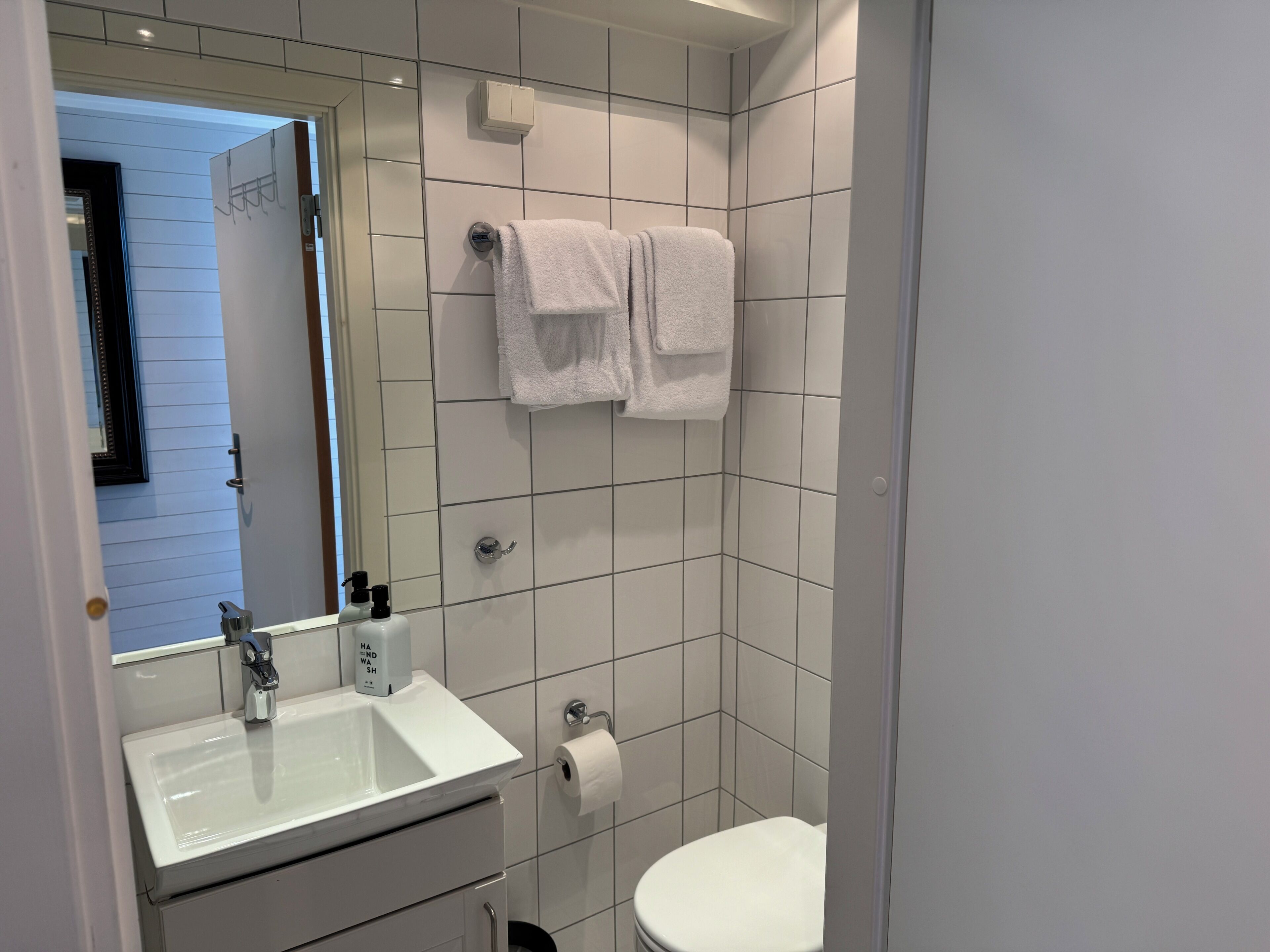 A bathroom with a sink, mirror, towel rack, toilet, and a door leading to another room.