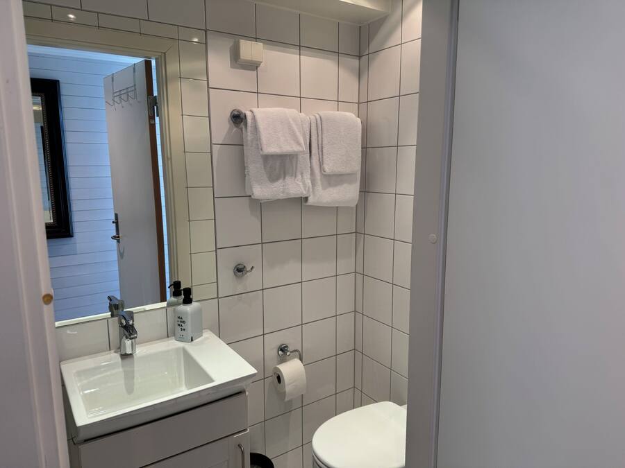 A bathroom with a sink, mirror, towel rack, toilet, and a door leading to another room.