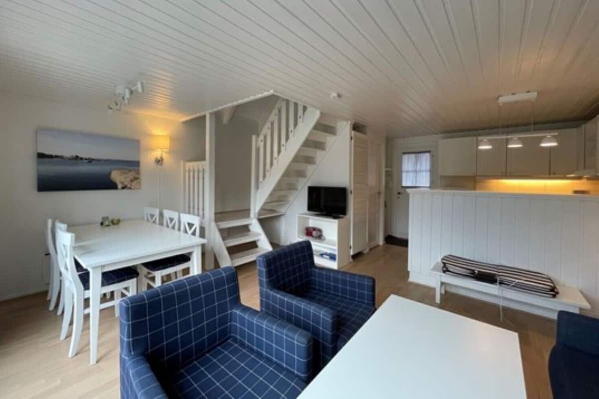 Ett kompakt bostadsutrymme med matplats, soffa, trappa och ett litet kök.