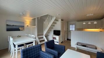 A compact living space with a dining area, sofa, staircase, and kitchenette.