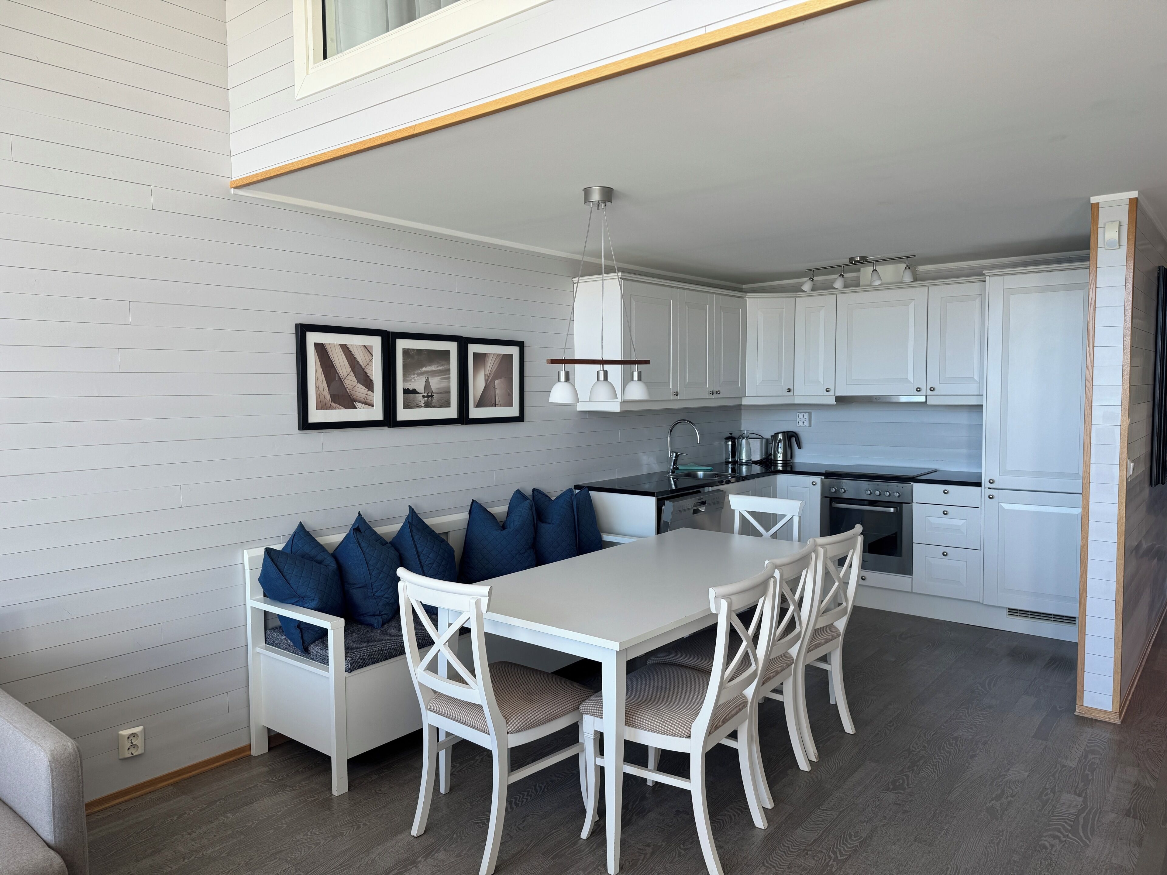 A modern kitchen with white cabinetry, a dining area with a white table and chairs, and a built-in bench with blue cushions.