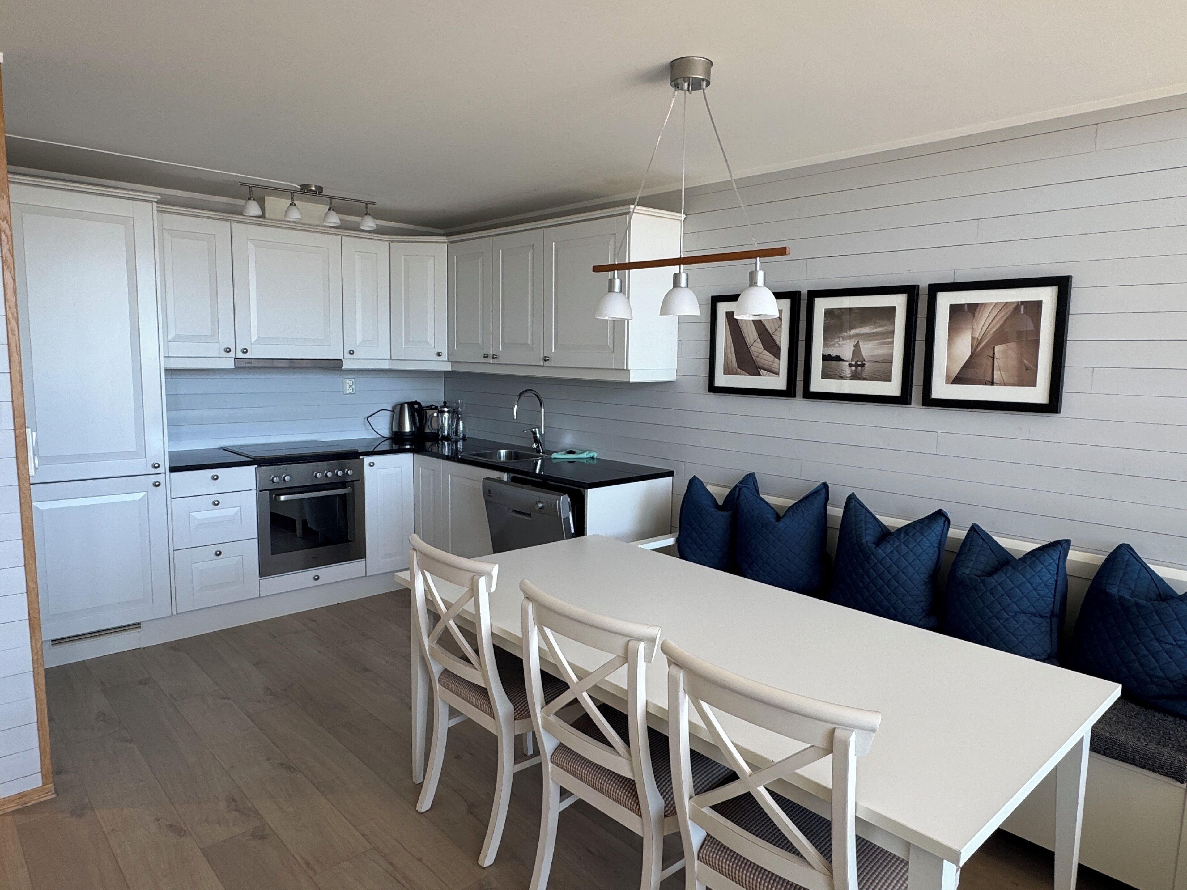 A modern kitchen with white cabinets, a dining table, and blue cushions on a sofa.
