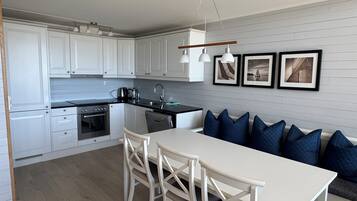 A modern kitchen with white cabinets, a dining table, and blue cushions on a sofa.