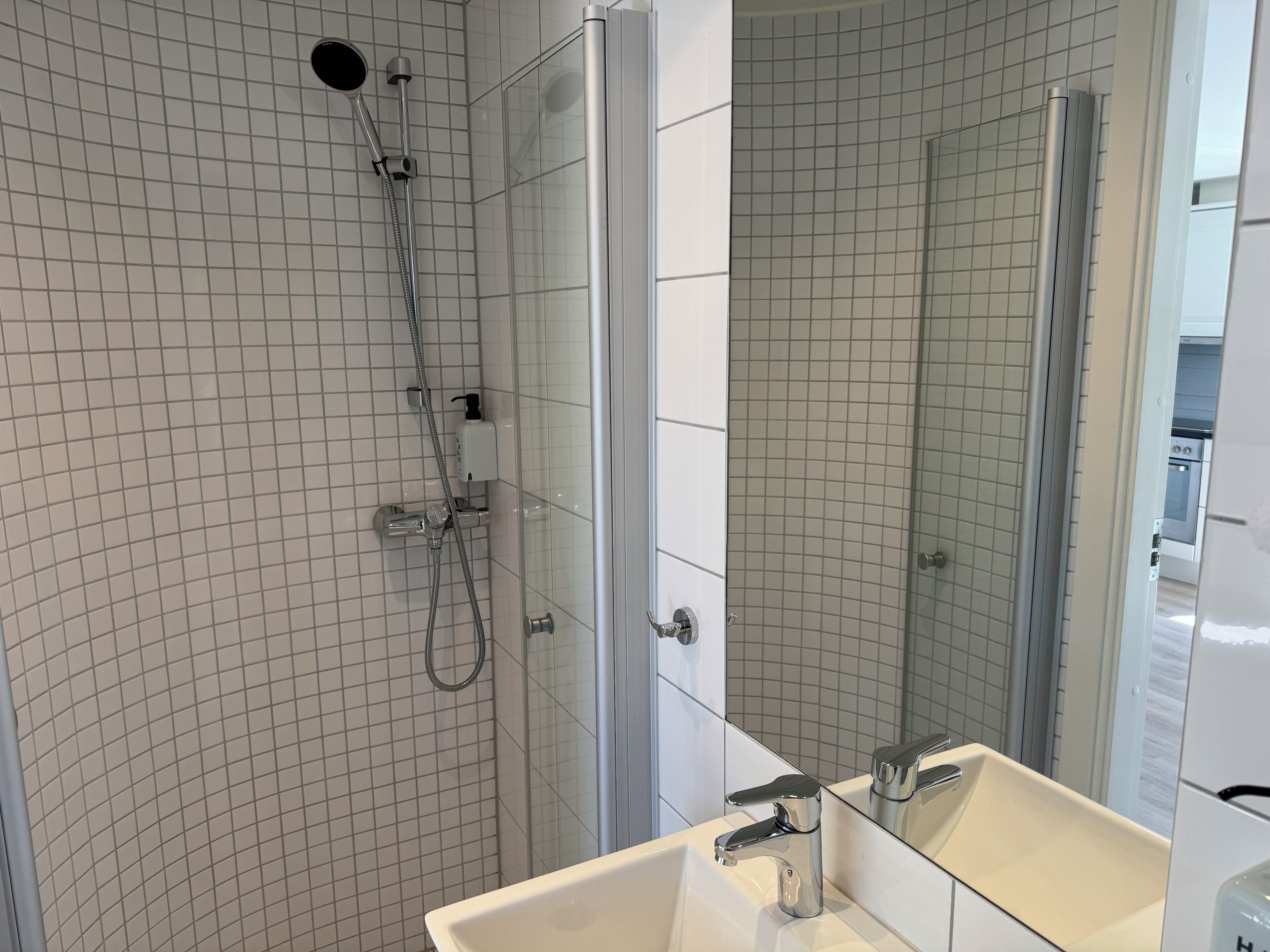 Un baño moderno con cabina de ducha de vidrio, un lavabo blanco y un espejo que refleja el ambiente.