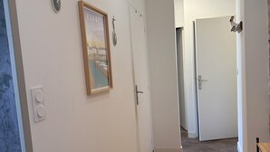 Un pasillo con suelo de madera, paredes blancas y una puerta que da a otra habitación.