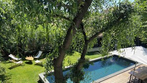 Ein Garten mit Swimmingpool, umgeben von einer Holzterrasse und einem Rasen. Liegestühle und ein Tisch mit Stühlen sind ebenfalls vorhanden.