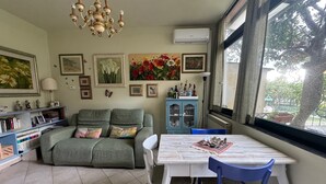 A cozy living room with a sofa, a dining table, and chairs. There are wall-mounted air conditioning units, a chandelier, and various framed pictures and decorations. - Casa Irene by the beach with garden and A/C (Monterosso al Mare)