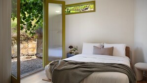 Une chambre à coucher avec un lit, une table de chevet, une lampe et une vue sur un jardin par la fenêtre.