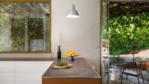 Une cuisine moderne avec une grande fenêtre, un luminaire suspendu, un bol de citrons et une petite plante posée sur le comptoir.
