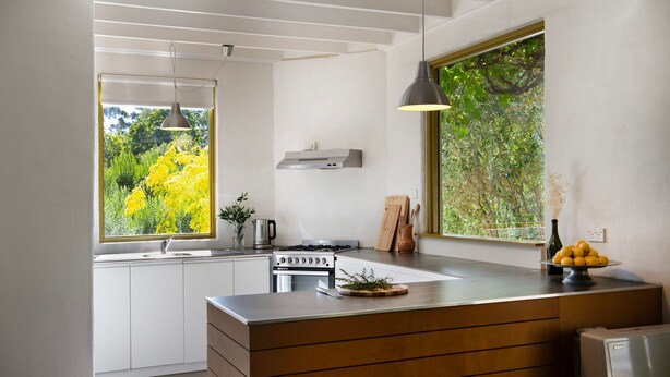 Une cuisine moderne dotée d’un îlot central, d’une cuisinière intégrée et d’une grande fenêtre donnant sur un paysage verdoyant.