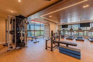 Ein Fitnessraum mit Trainingsgeräten, einer Bank und großen Fenstern.