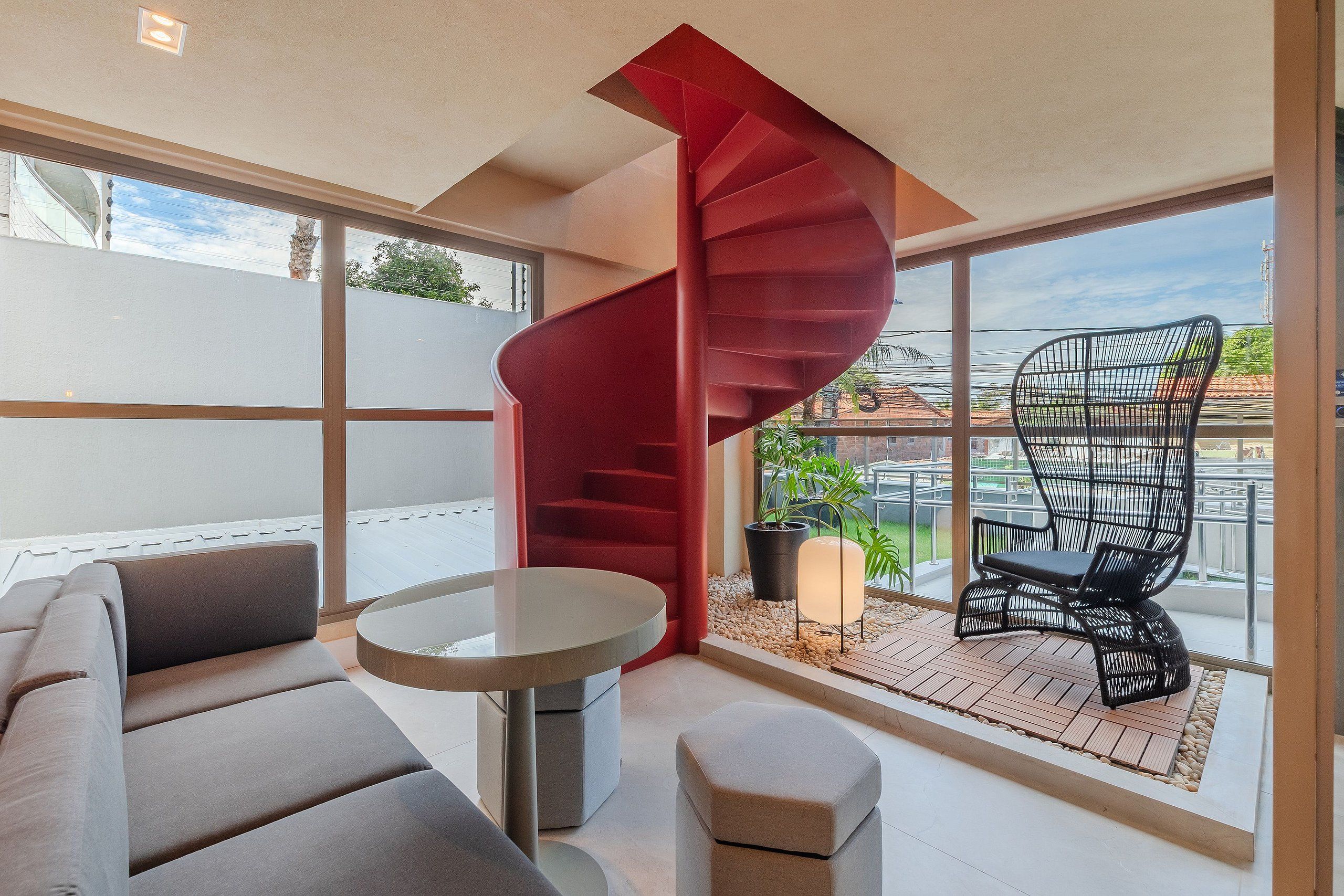 Un interior moderno con una escalera de caracol, un sofá, una mesa redonda y un balcón con una silla y plantas.