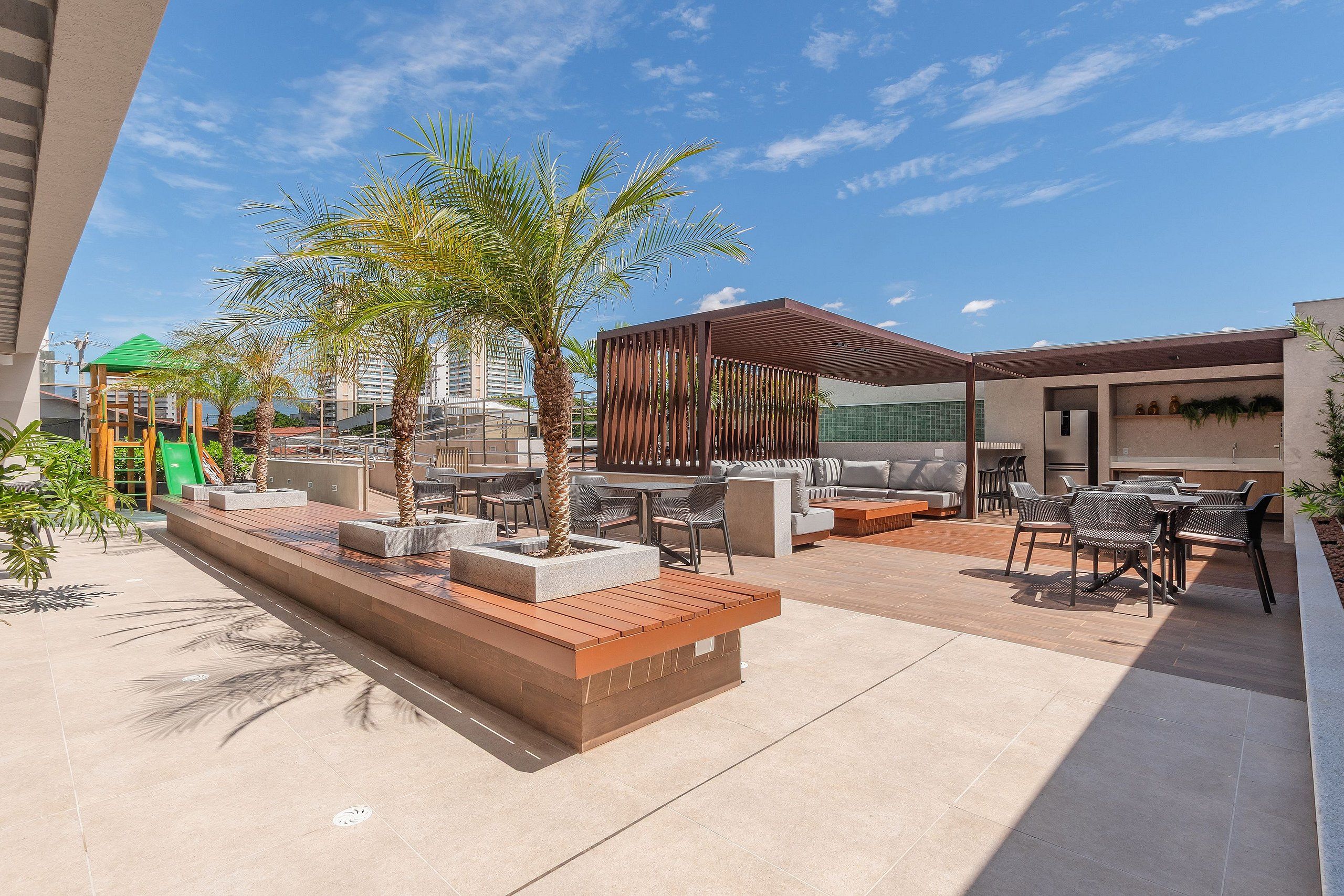 Un patio al aire libre con mobiliario, palmeras y un parque infantil.