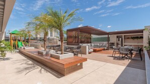 Un patio al aire libre con mobiliario, palmeras y un parque infantil.