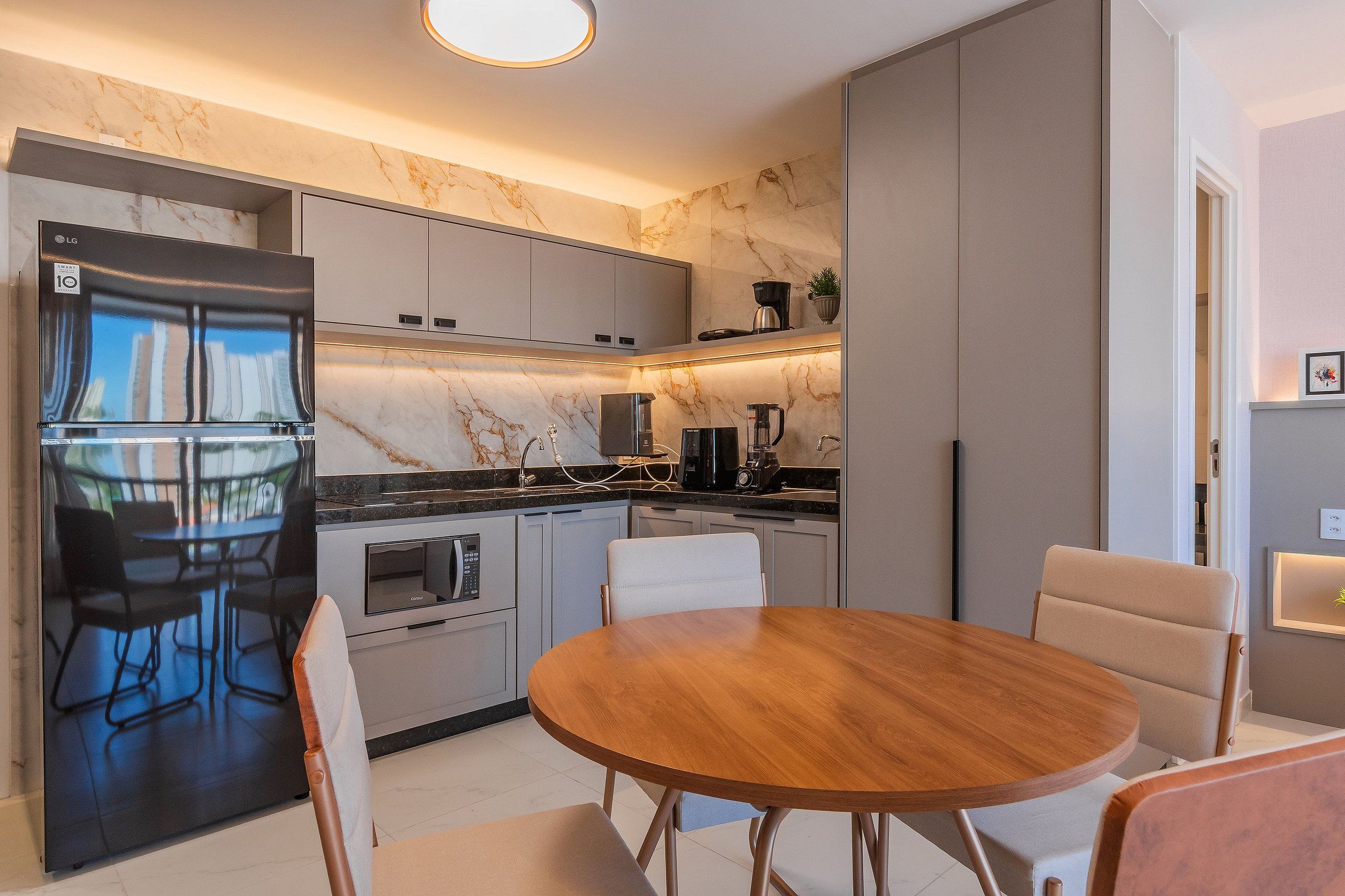A modern kitchen with a built-in refrigerator, microwave, and oven. There is a round wooden table with chairs, and a small potted plant on the countertop.