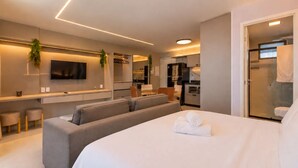 Una habitación de hotel moderna con una cama grande, un área de estar, una kitchenette y un televisor.