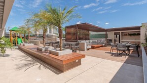 Eine Außenpatio-Terrasse mit Sitzgelegenheiten, Palmen und einer Spielanlage.