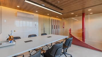 Una sala conferenze con un lungo tavolo, sedie nere, una lavagna e una parete rossa che fa da elemento decorativo.