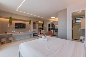A modern hotel room with a large bed, a TV, a seating area with chairs, a small table, and a glass shower enclosure.