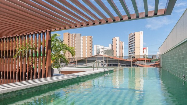 Una piscina con agua cristalina, rodeada por una estructura de pérgola y con vistas a edificios altos al fondo.