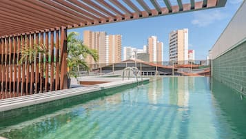 Una piscina con agua cristalina, rodeada por una estructura de pérgola y con vistas a edificios altos al fondo.