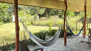 A covered outdoor area with a stone floor, a hammock, and a wooden chair. - Peaceful campground in Monteverde perfect for nature lovers (San Luis de Monteverde)
